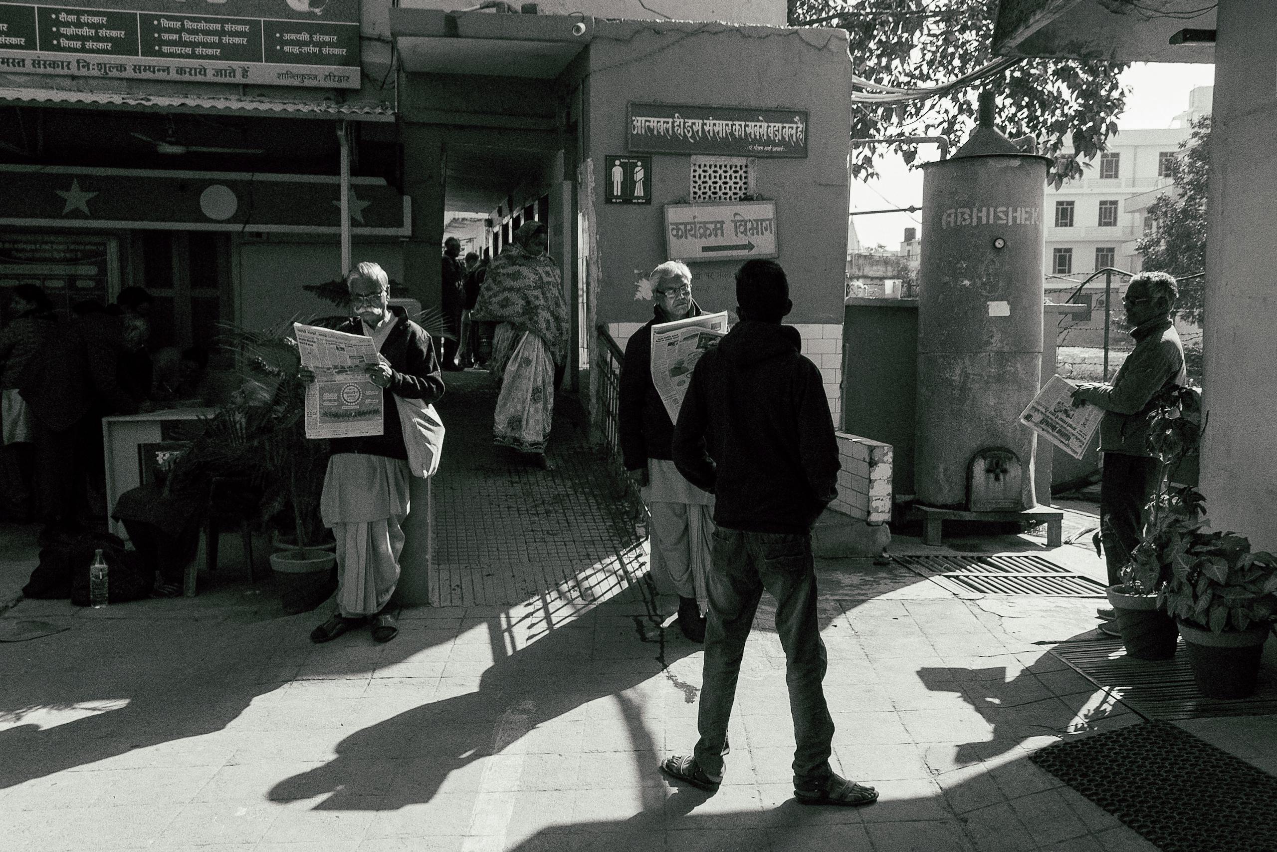 Black and white of serious men in casual clothes standing on street and reading notes in newspapers