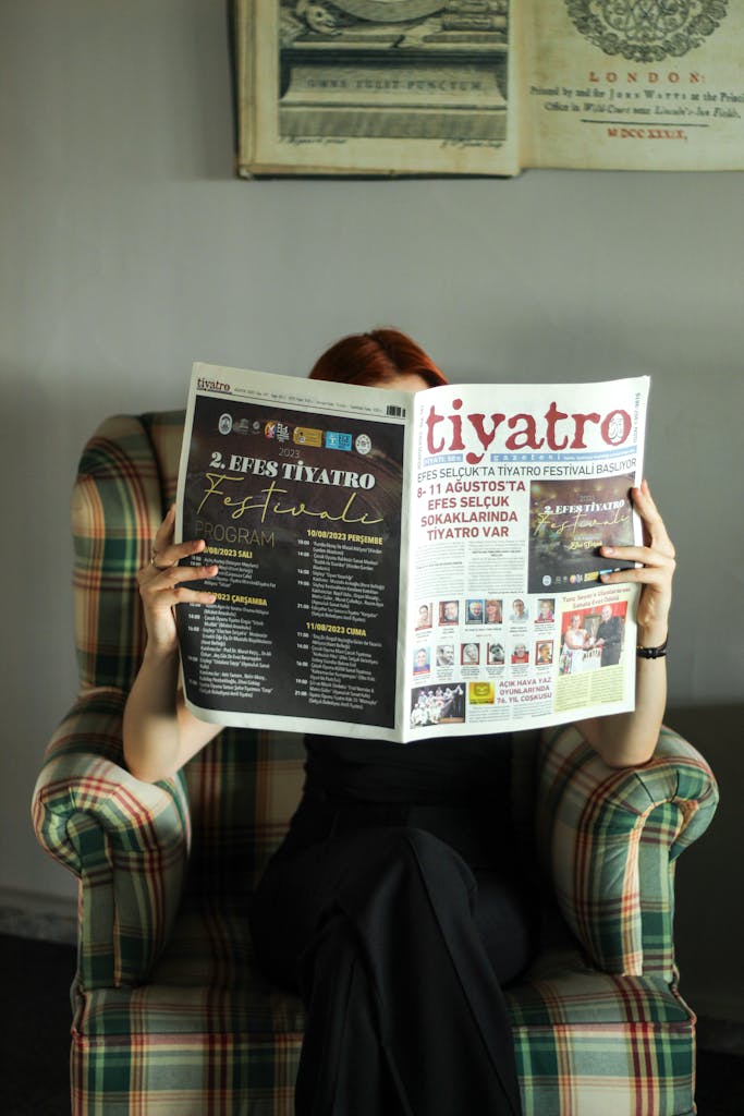 A woman sits in a cozy armchair reading a newspaper, creating a retro and relaxed atmosphere.