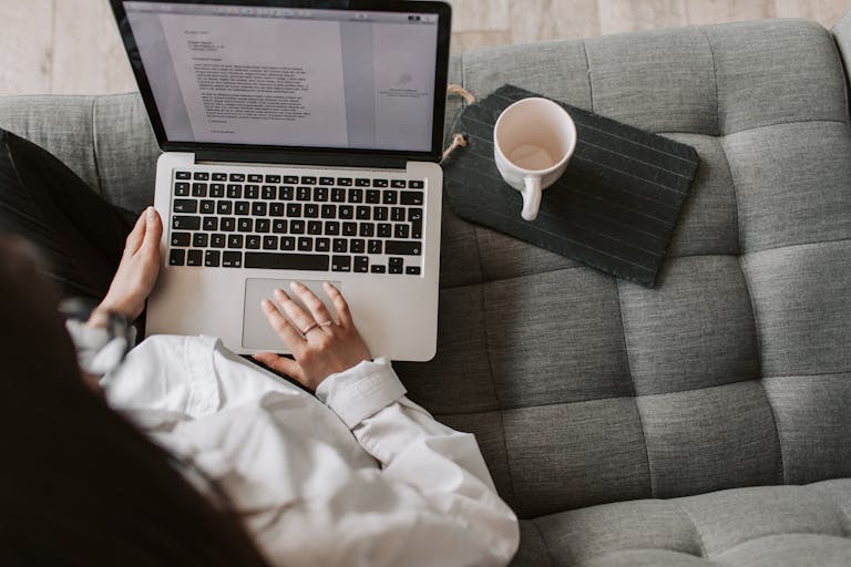 From aboveDailyMagazineWorld: Redefining Digital Journalism in the Modern Age of woman in casual wear sitting on comfortable couch with cup and typing on keyboard of laptop while working remotely in cozy living room
