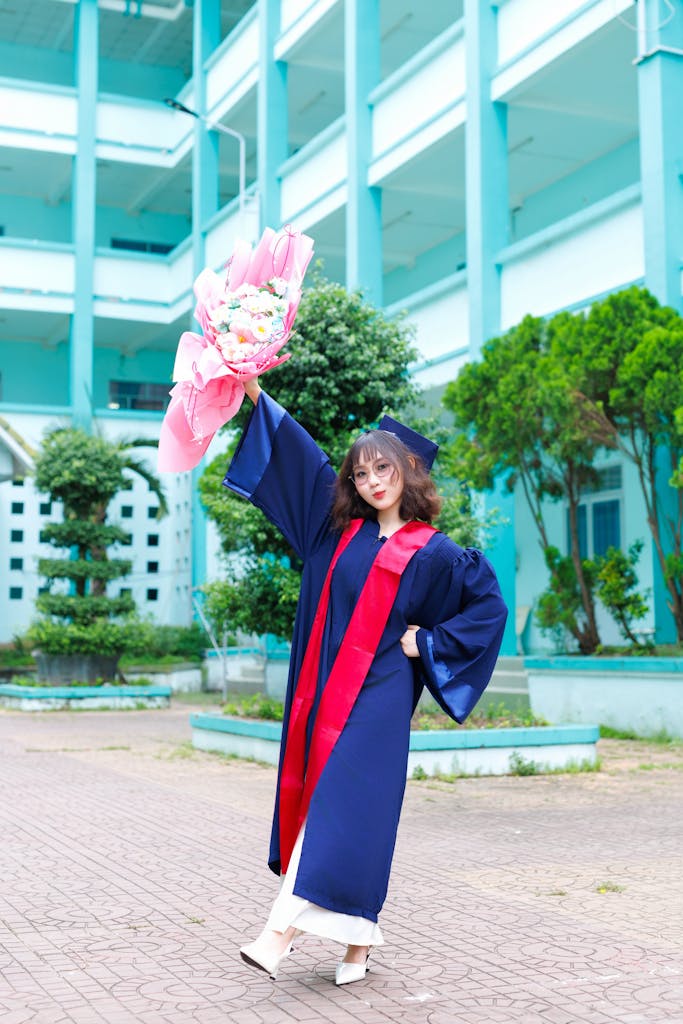 Happy female graduate in cap and gown celebrates with a bouquet outdoors.