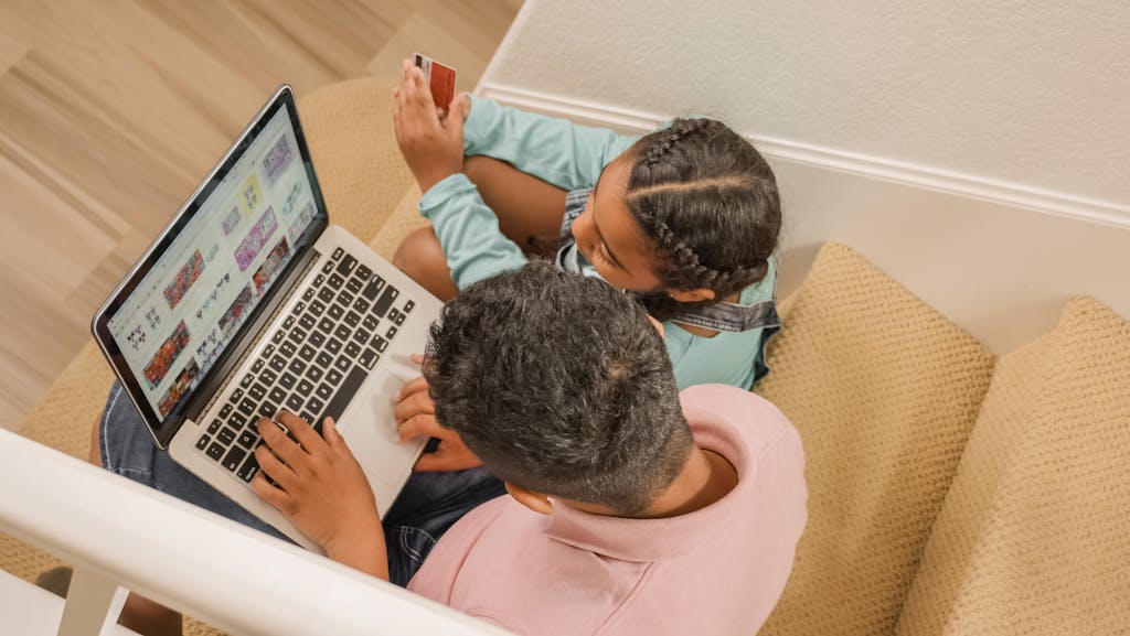 Messagenal Mansutfer A father and daughter sit on stairs, engaging in online shopping together using a laptop.