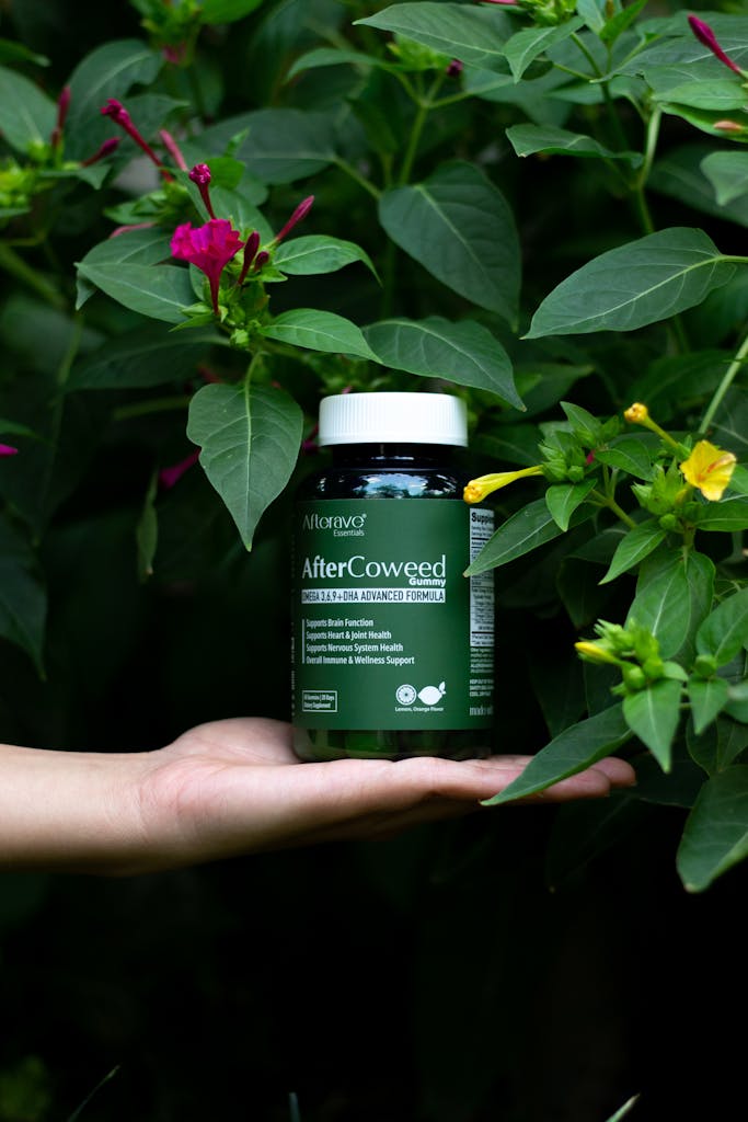 A hand holds a herbal supplement bottle amidst vibrant green foliage, promoting natural wellness.