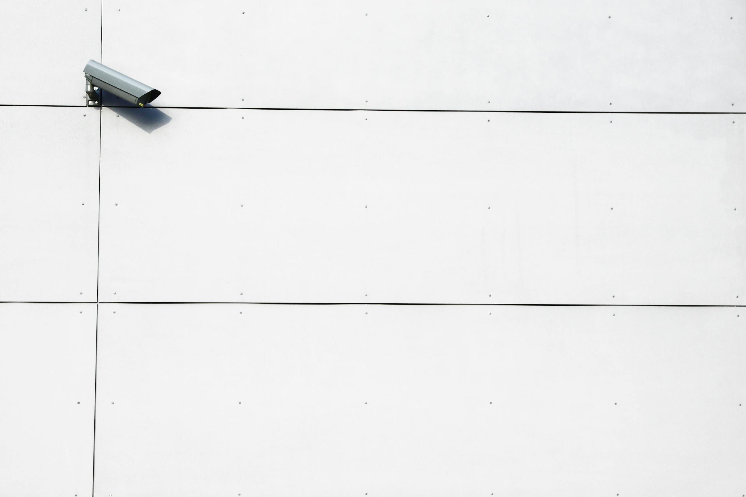 ReadSpeak A minimalist image showcasing a single surveillance camera mounted on a stark white wall.