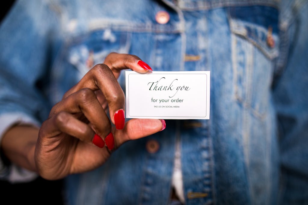 Sodiceram A woman in a denim jacket holds a 'Thank You' card with red nails.
