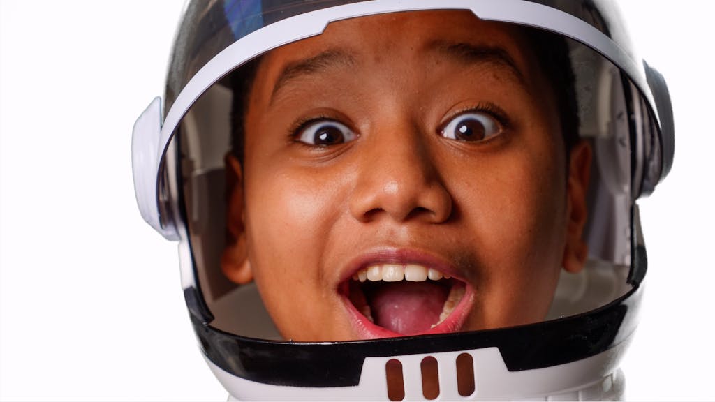 Close-up of a joyful child wearing a space helmet, expressing excitement and wonder.
