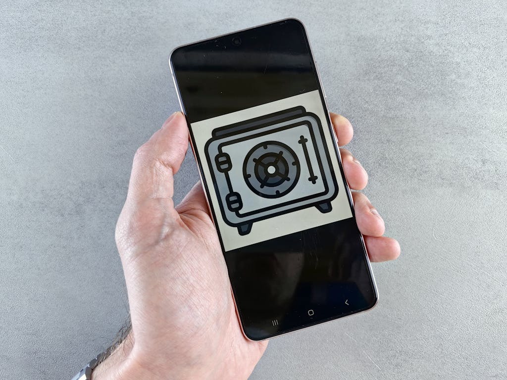 Juntos Seguros Close-up of a smartphone showing a safe icon held in a hand, symbolizing digital security.