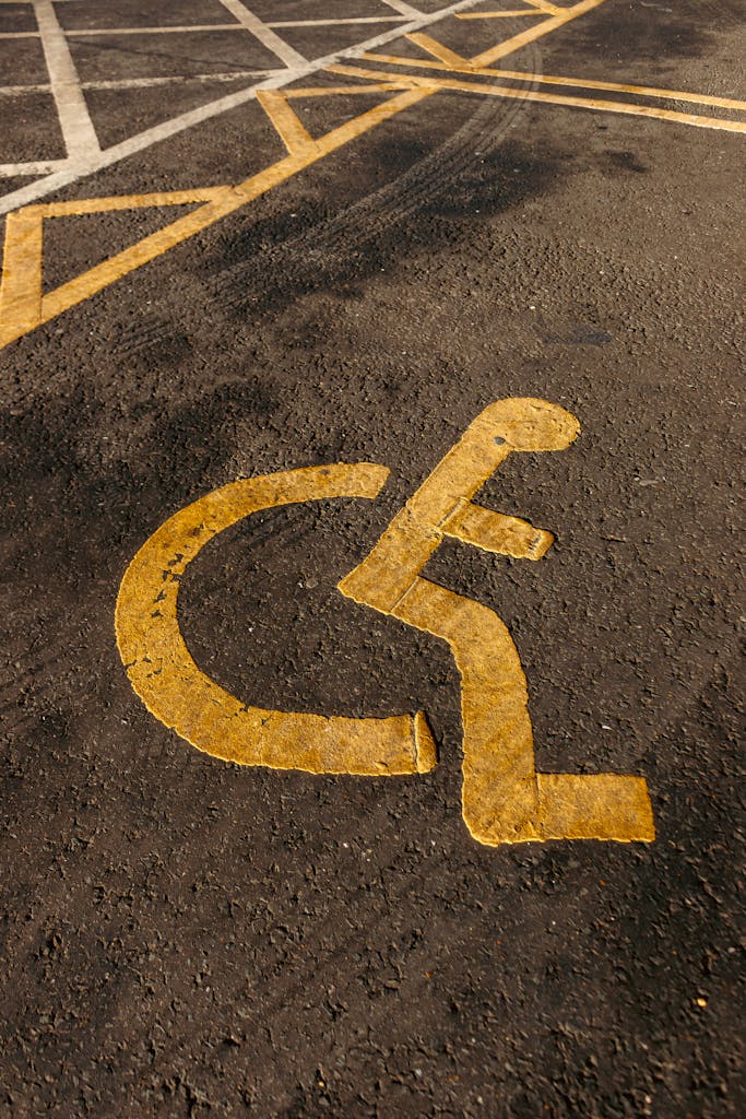 Close-up of a yellow disabled parking symbol on asphalt pavement with textured surface.