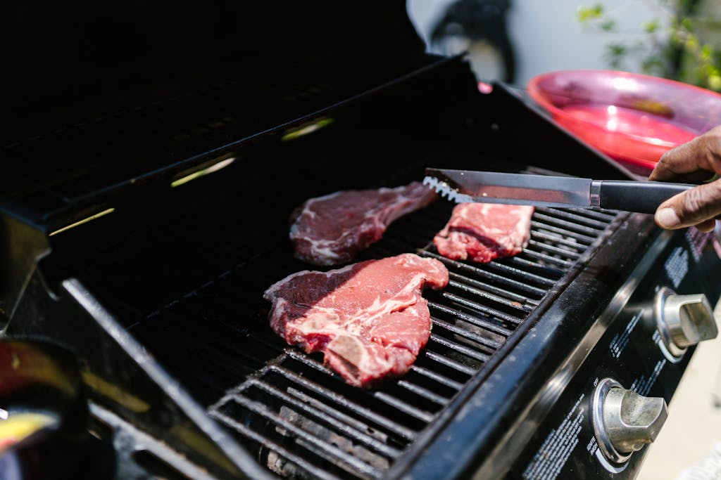 Weber Grillvorführung Close-up of juicy steaks on an outdoor grill, held with tongs, perfect for barbecue enthusiasts.