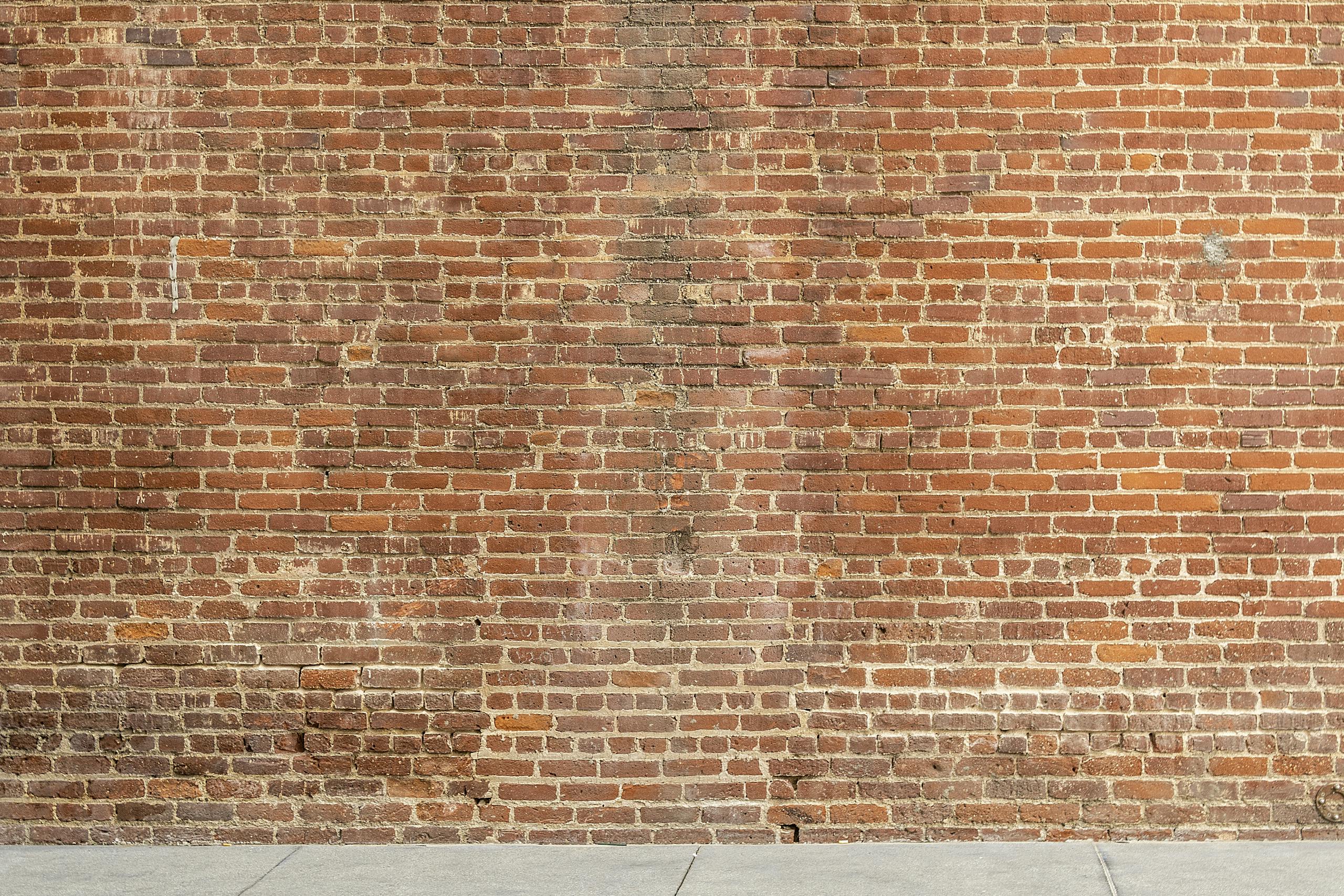 Sixmagazine Detailed image of a textured red brick wall with a concrete base, ideal for architectural and design backgrounds.
