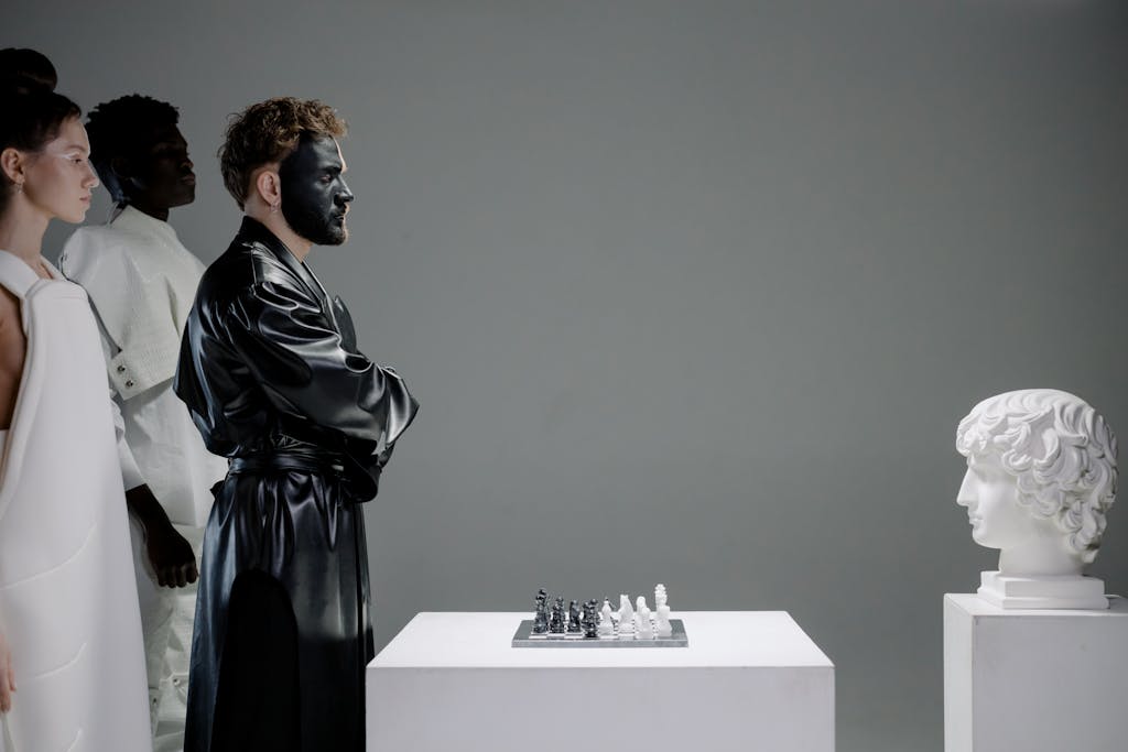 Dramatic studio portrayal of chess game, featuring performers in costume and face paint, alongside a classic sculpture.