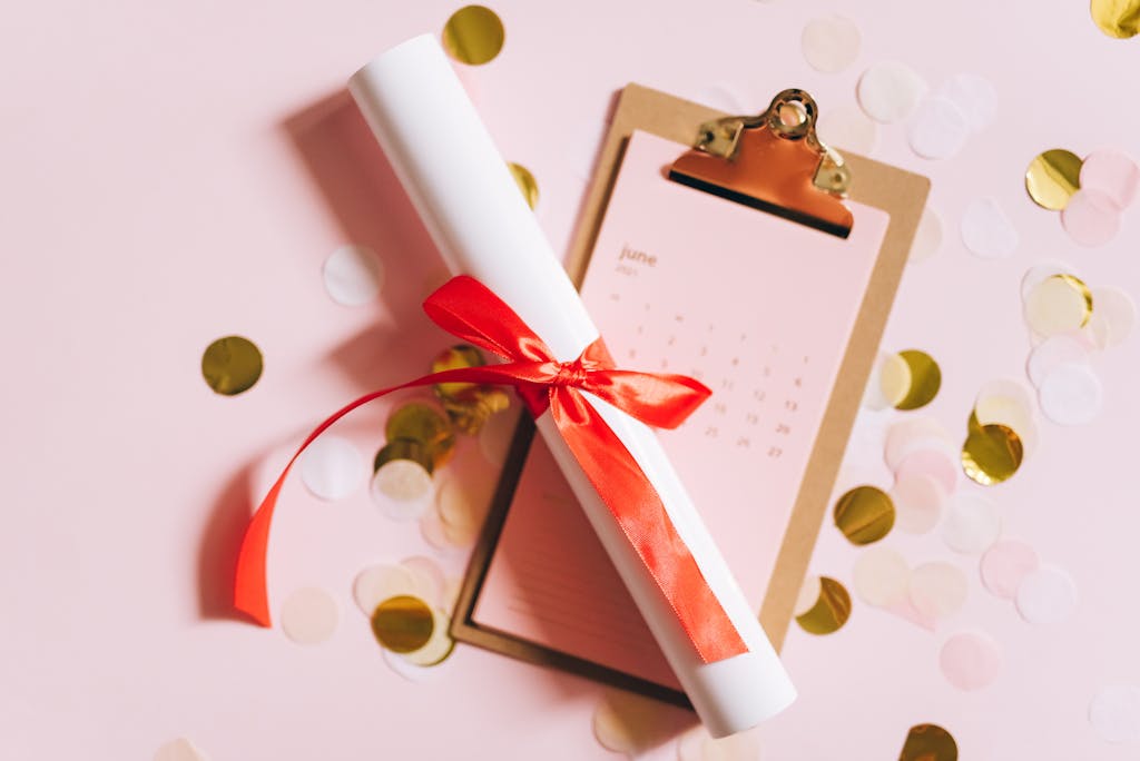 Six Sigma Certification Online Flat lay of a graduation diploma with a red ribbon on a clipboard with confetti.