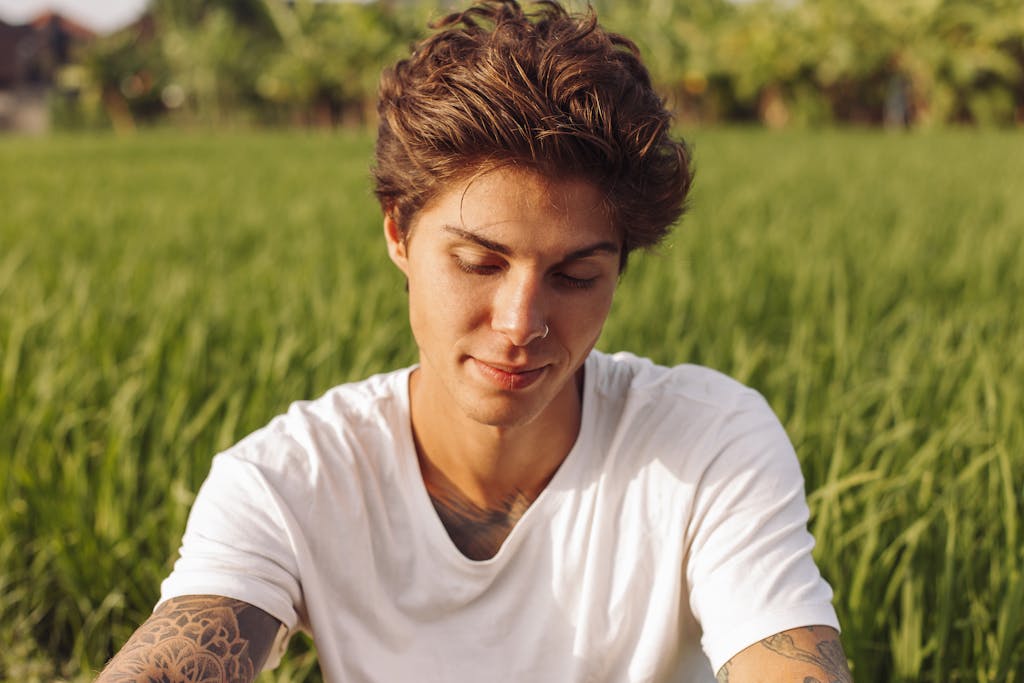 Portrait of a young man with tattoos relaxing in a sunny green field.