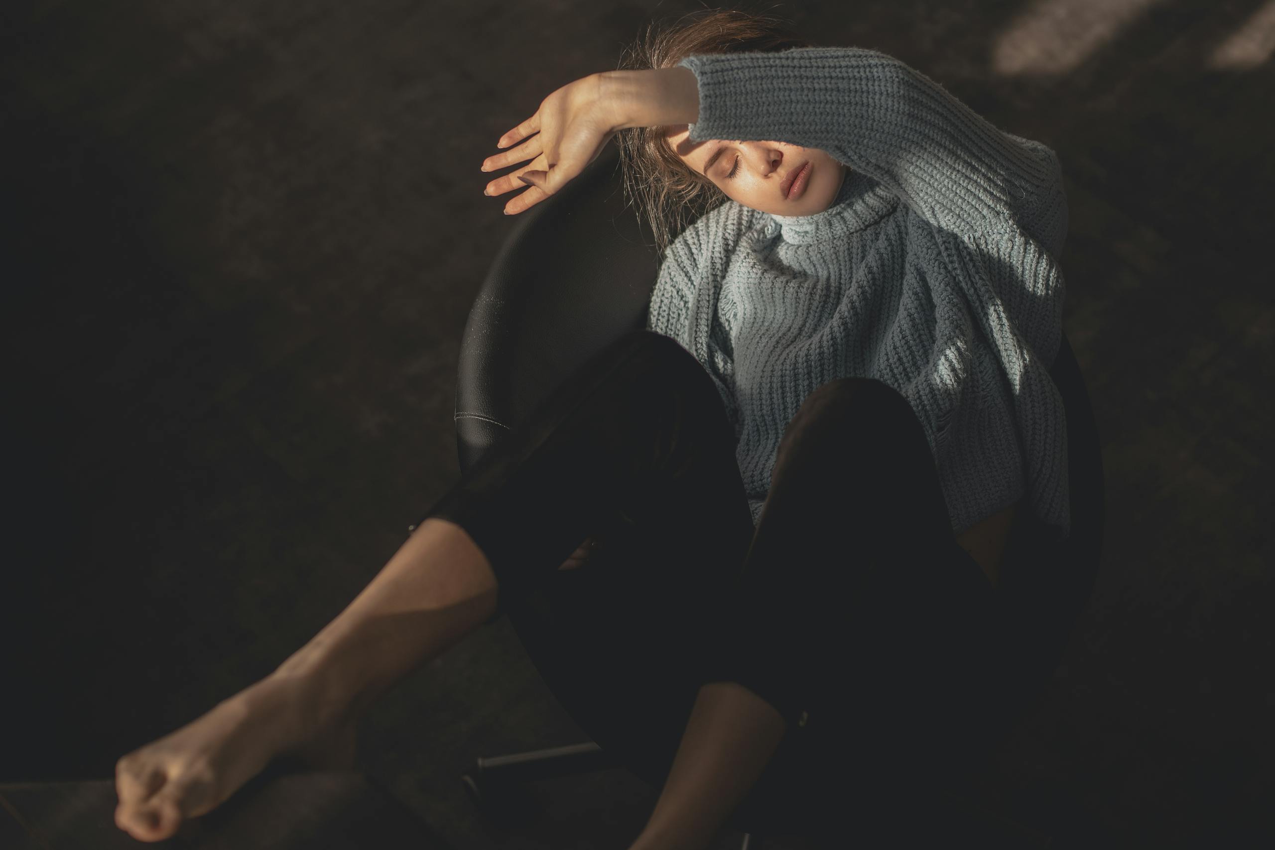 Carmela Clouth young woman in a cozy sweater, relaxing indoors on a chair with a modern, fashionable look.