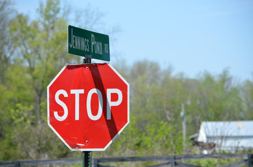 Technewstop.org A stop sign and road sign on Jennings Pond Road in a rural setting with trees and blue sky.