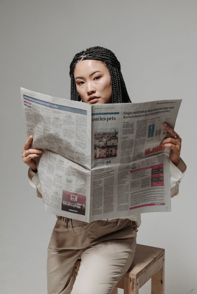 Newscrane A stylish woman with braided hair reading a newspaper in a studio setting.