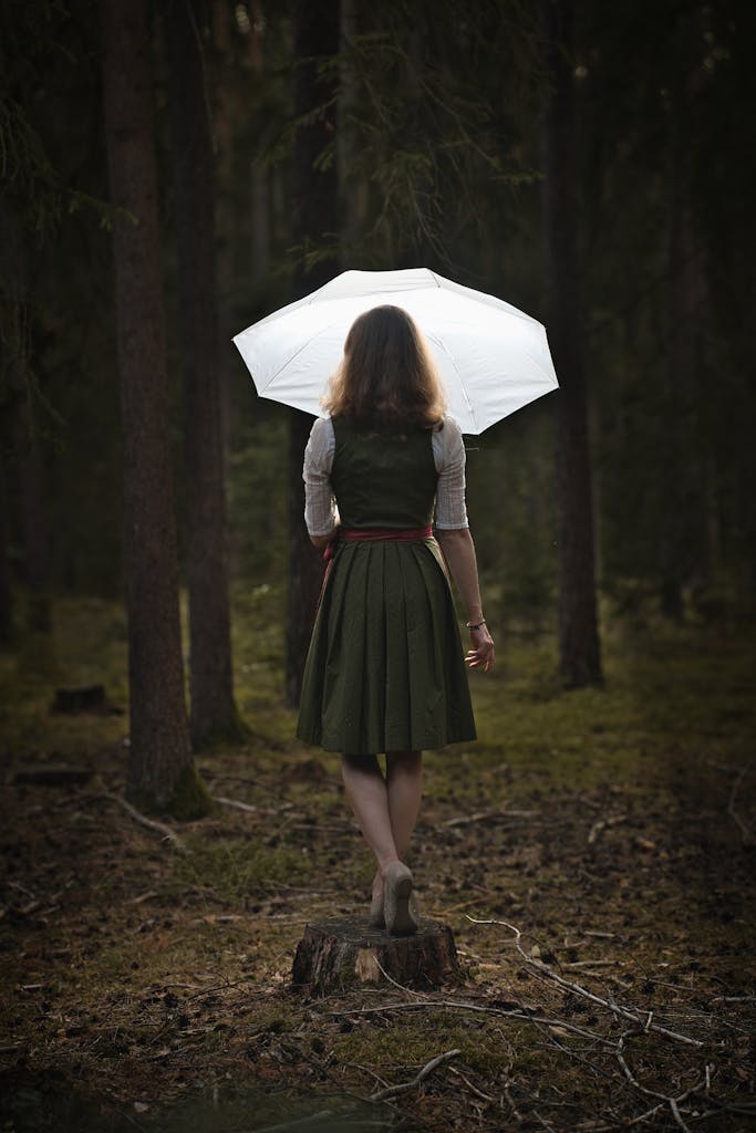 Uitly A woman in traditional attire stands on a tree stump holding an umbrella in a German forest.