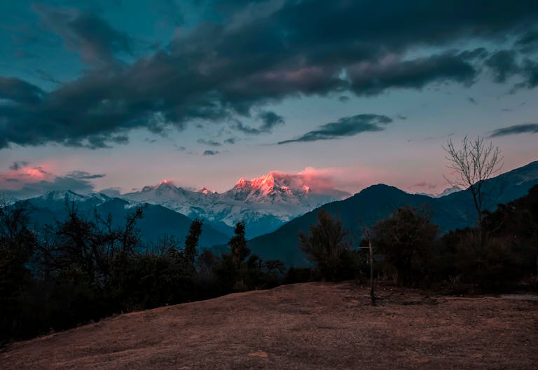 Otsnews.co.uk Breathtaking view of snowcapped mountains glowing under a twilight sky with rich cloud formations.