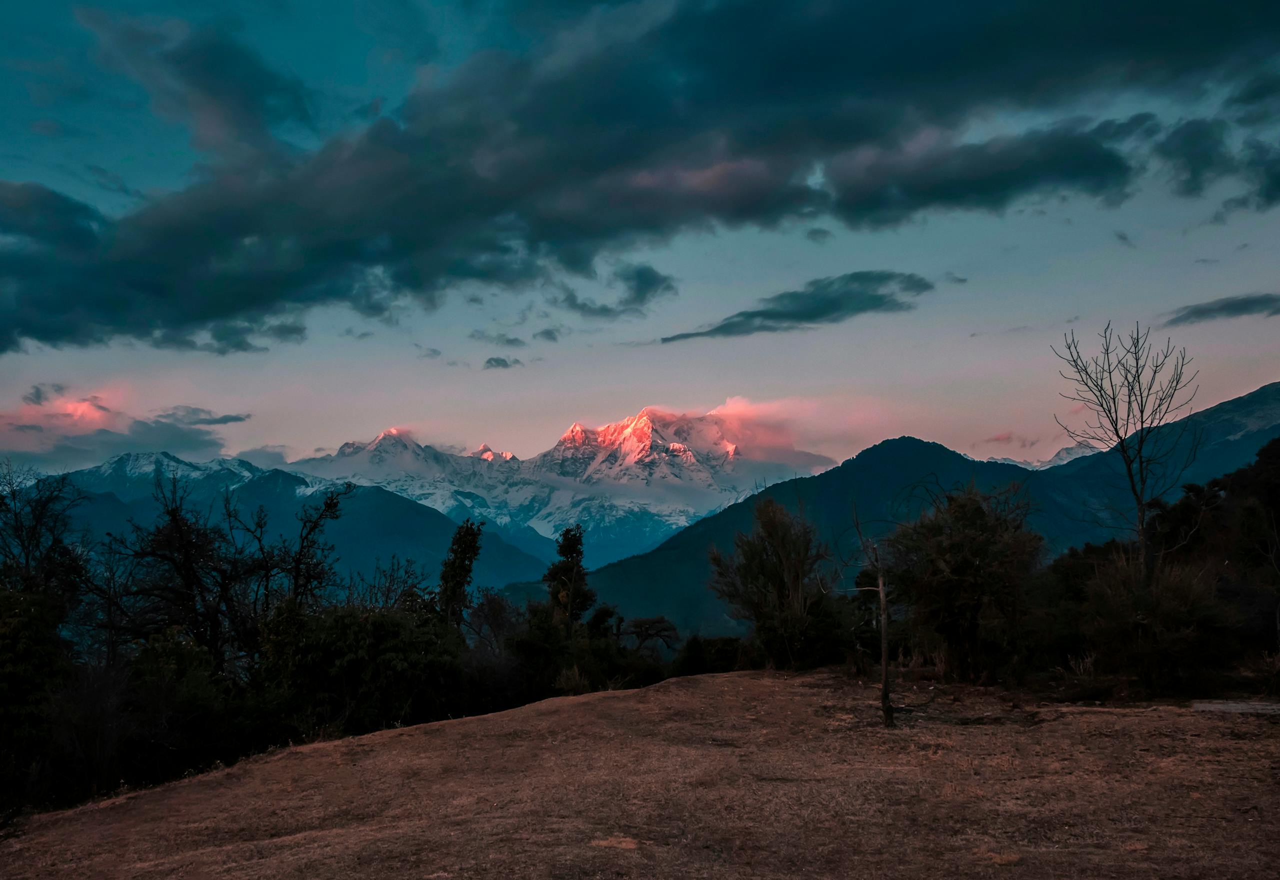 Otsnews.co.uk Breathtaking view of snowcapped mountains glowing under a twilight sky with rich cloud formations.
