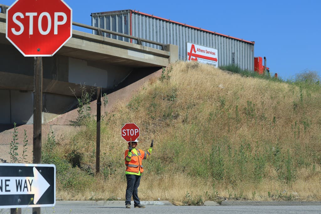 Technewstop.org Construction worker with stop sign managing traffic near a bridge.