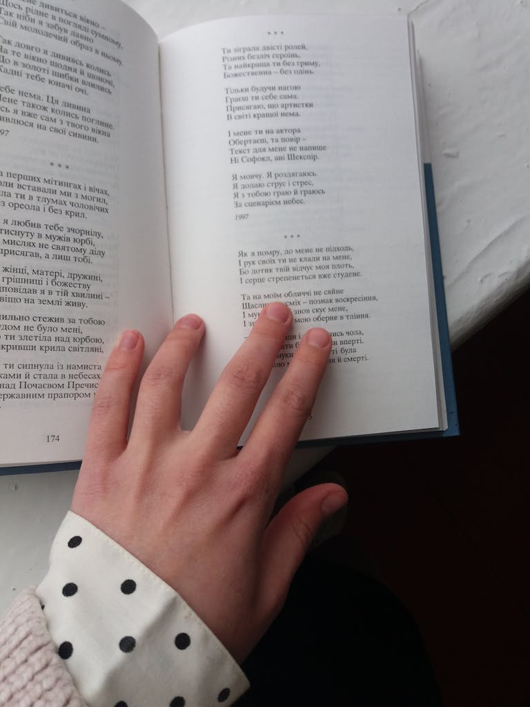 Uitly Hand placed on an open book displaying printed text on a table.
