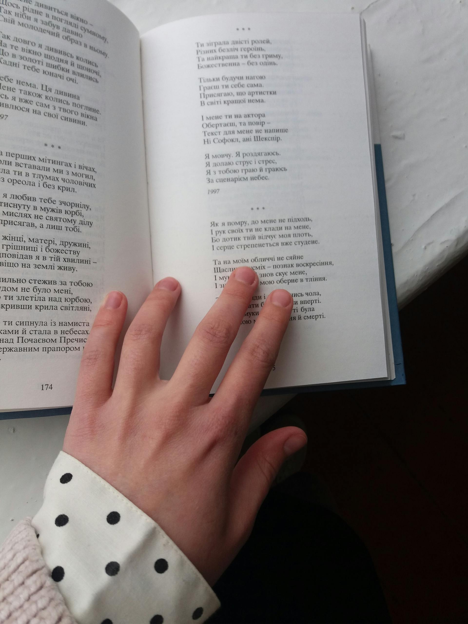 Uitly Hand placed on an open book displaying printed text on a table.
