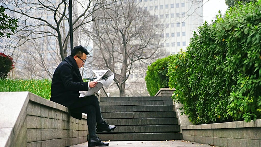 IntelligentNews.co.uk Man reading newspaper outdoors on a park bench during a peaceful afternoon break.