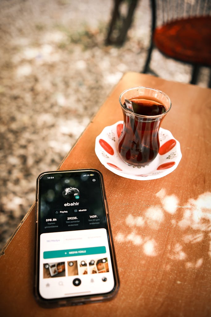 veb vatsap com Mobile phone beside traditional Turkish tea on an outdoor wooden table.