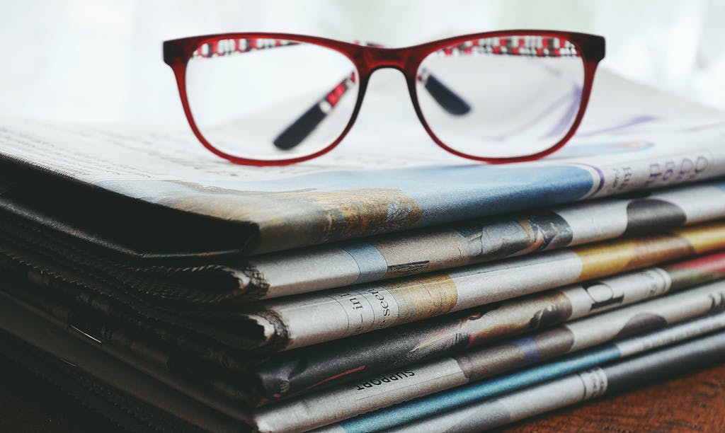 DailyNewsWork.com Red glasses on stacked newspapers.