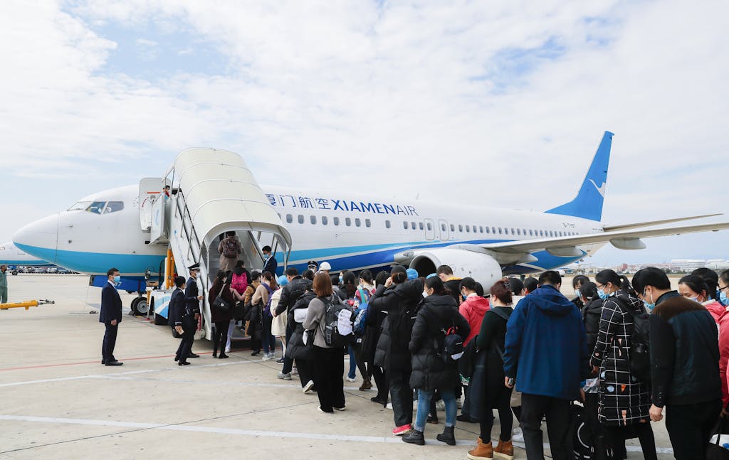 TOpenskynews ravelers at an airport embarking a XiamenAir plane on a clear day.