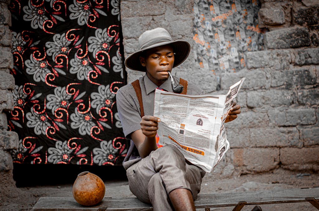 Newscora A man in traditional attire reads a newspaper against a vibrant backdrop in Blantyre, Malawi.