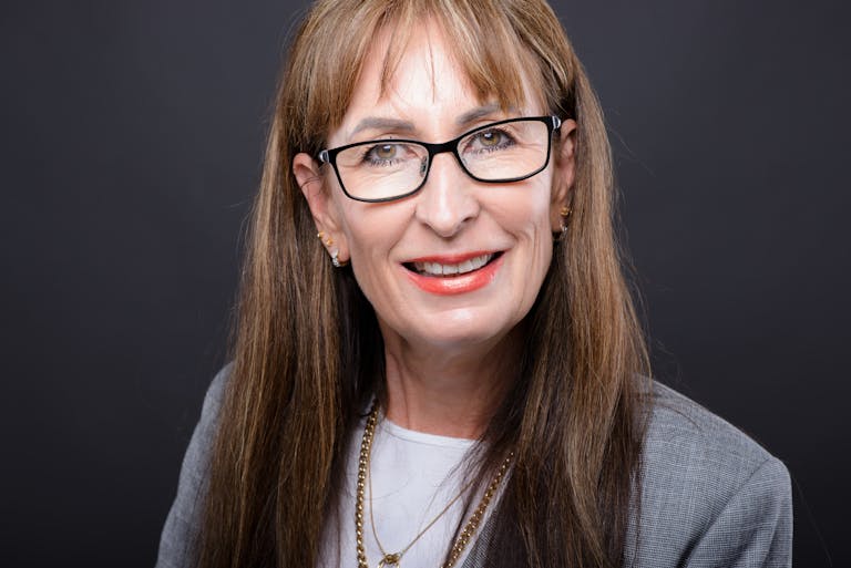 Wendy Etris A senior woman smiling in eyeglasses and a gray coat, with a confident expression.