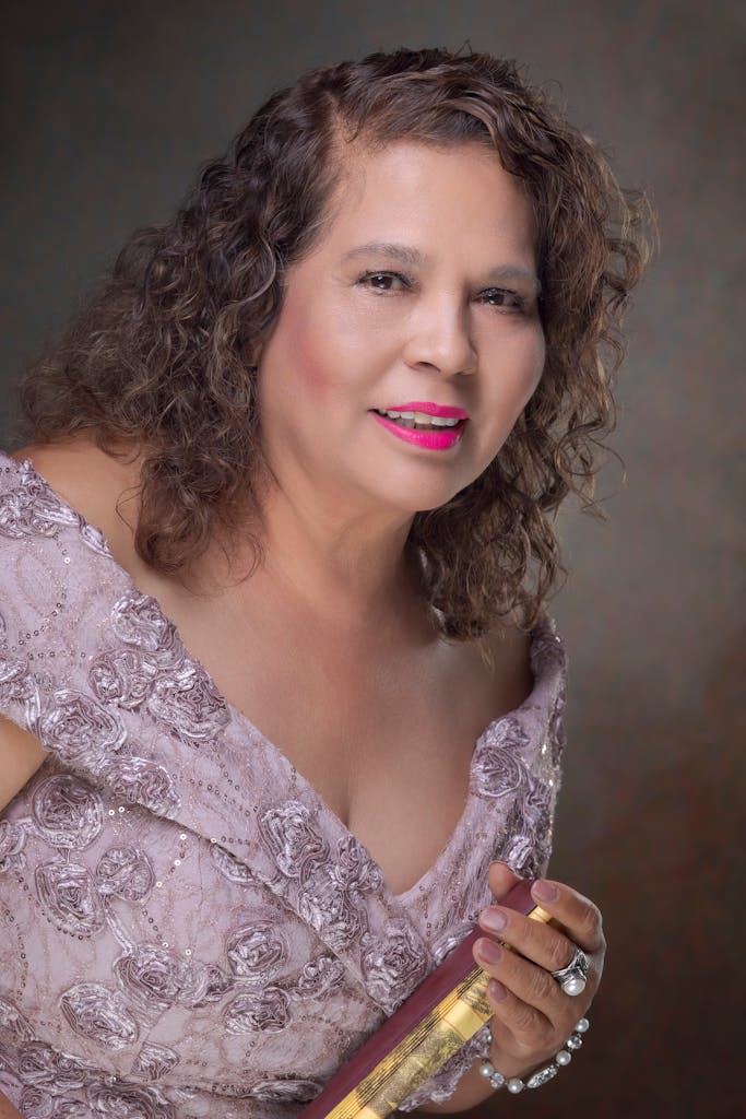 Lupe Gidley Sophisticated portrait of an adult woman in a floral pink dress with curly hair.