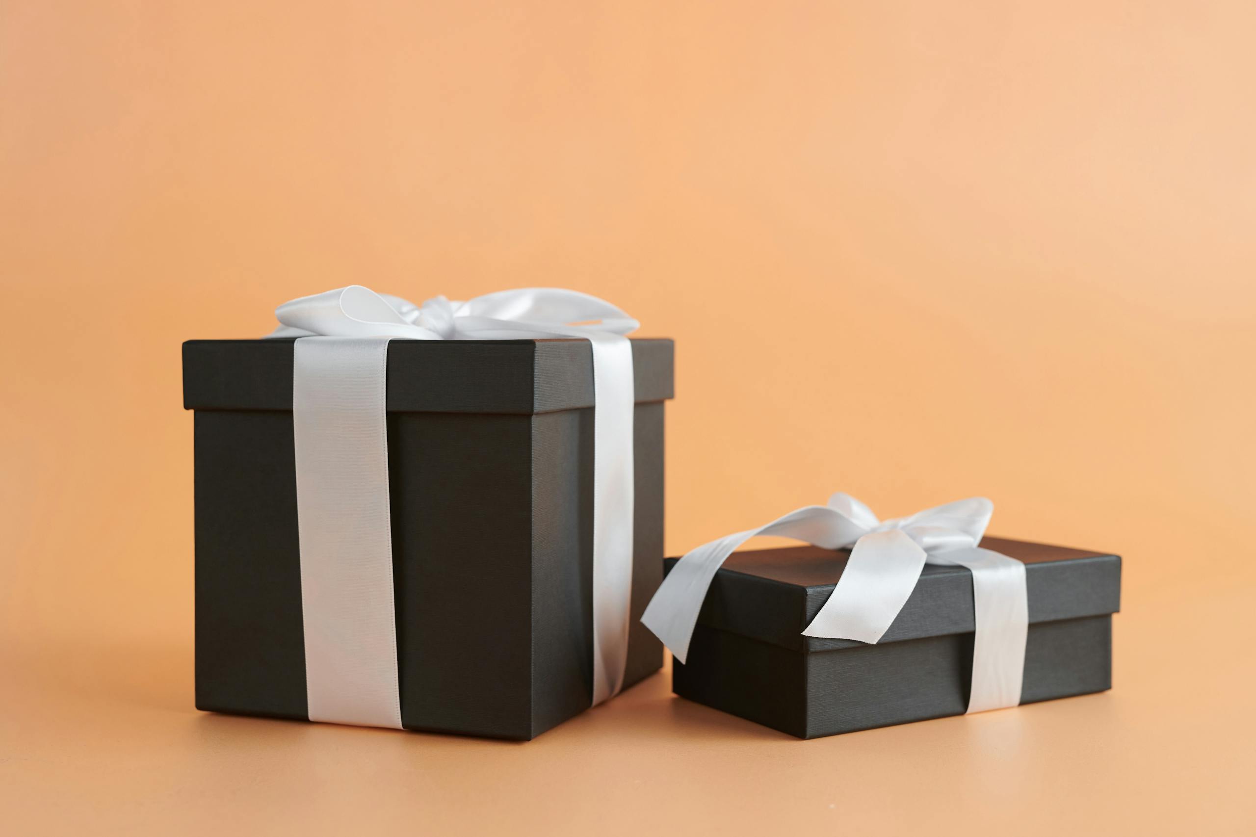 WhatUTalkingBoutWillis Gifts Two black gift boxes with white ribbons on a beige background, perfect for celebrations.