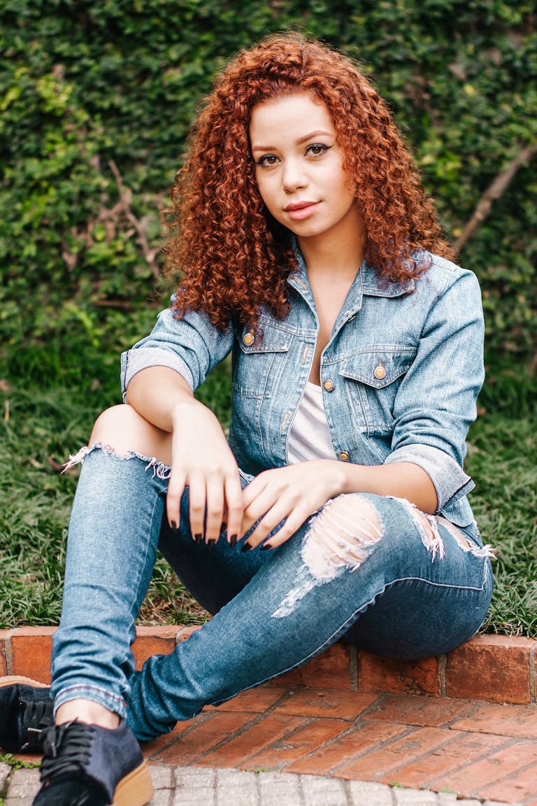 Laryssa Farmiga Young woman in denim jacket and jeans sitting outdoors, exuding casual chic style.