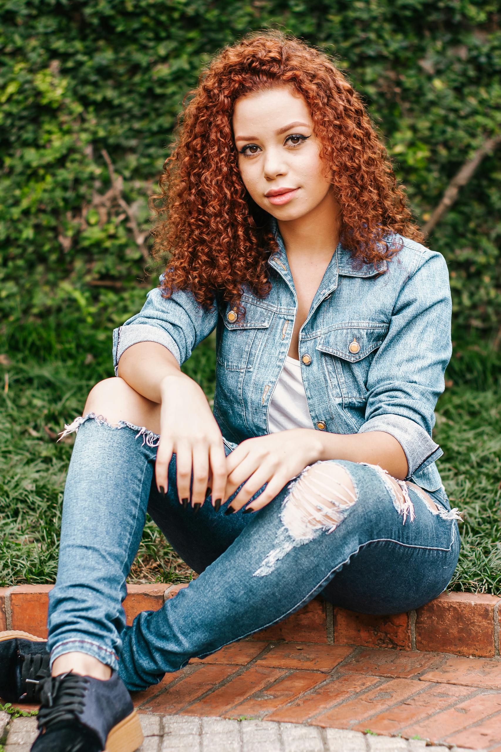 Laryssa Farmiga Young woman in denim jacket and jeans sitting outdoors, exuding casual chic style.